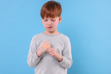 Photo of Little boy putting sticking plaster onto hand on light blue background