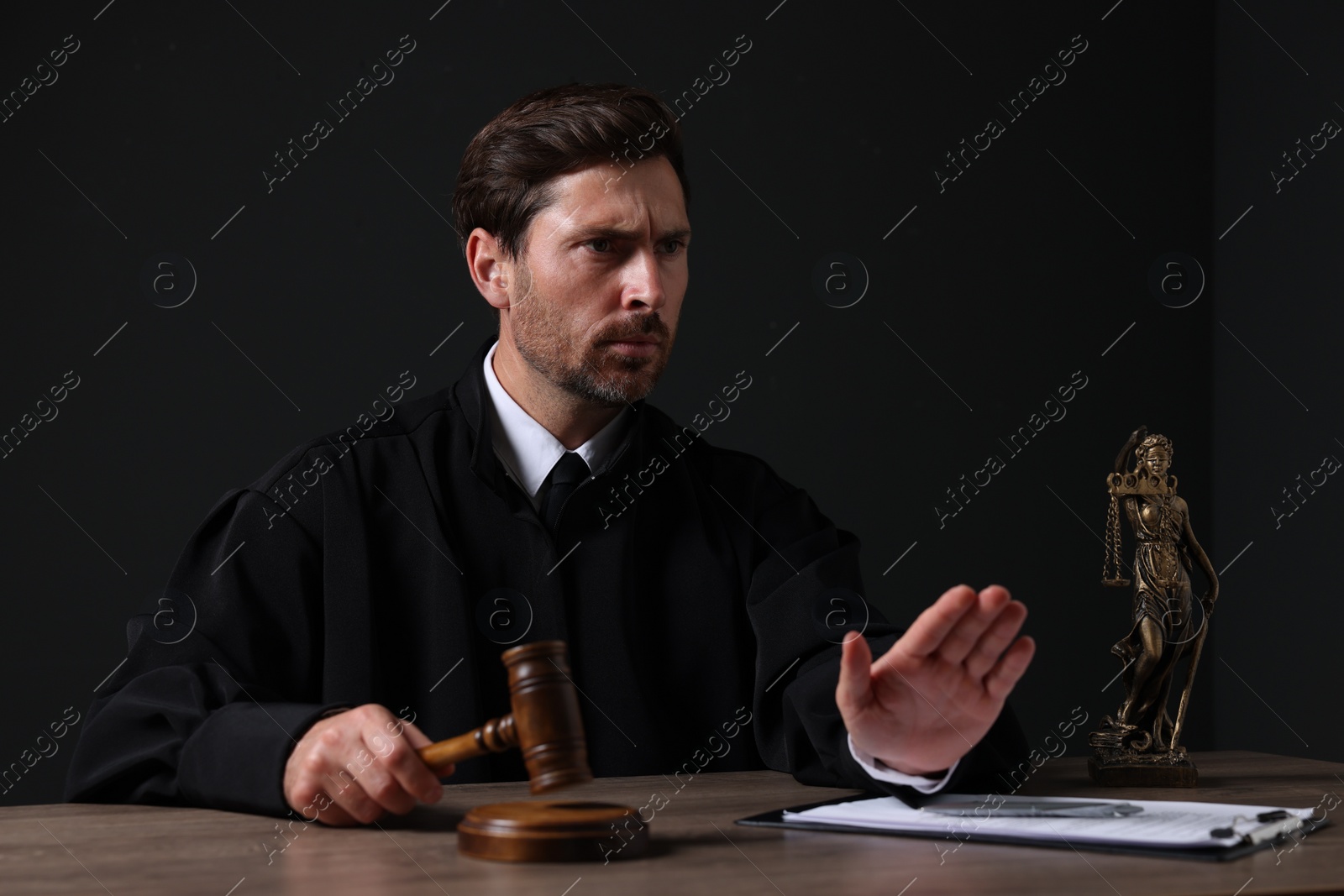 Photo of Judge with gavel and papers sitting at wooden table against black background