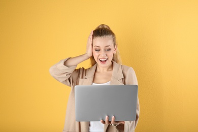 Portrait of emotional young woman with laptop on yellow background