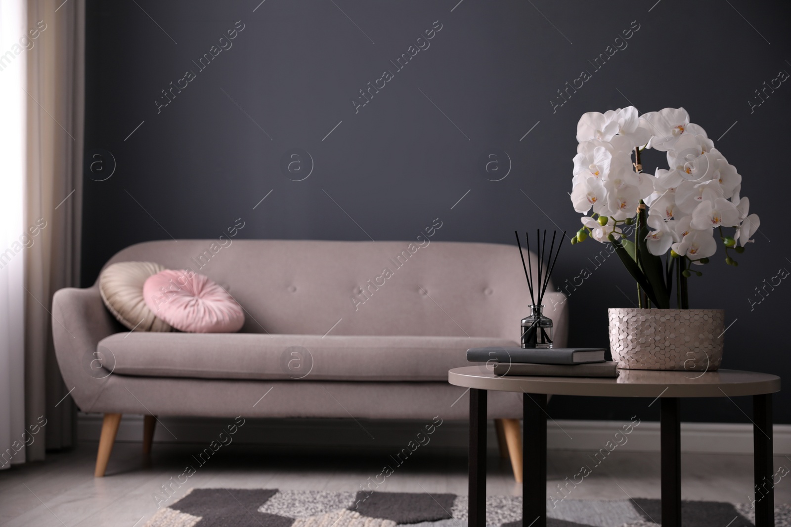 Photo of Beautiful orchid, books and air reed freshener on table indoors