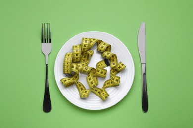 Photo of Measuring tape, fork and knife on light green background, flat lay. Weight loss concept