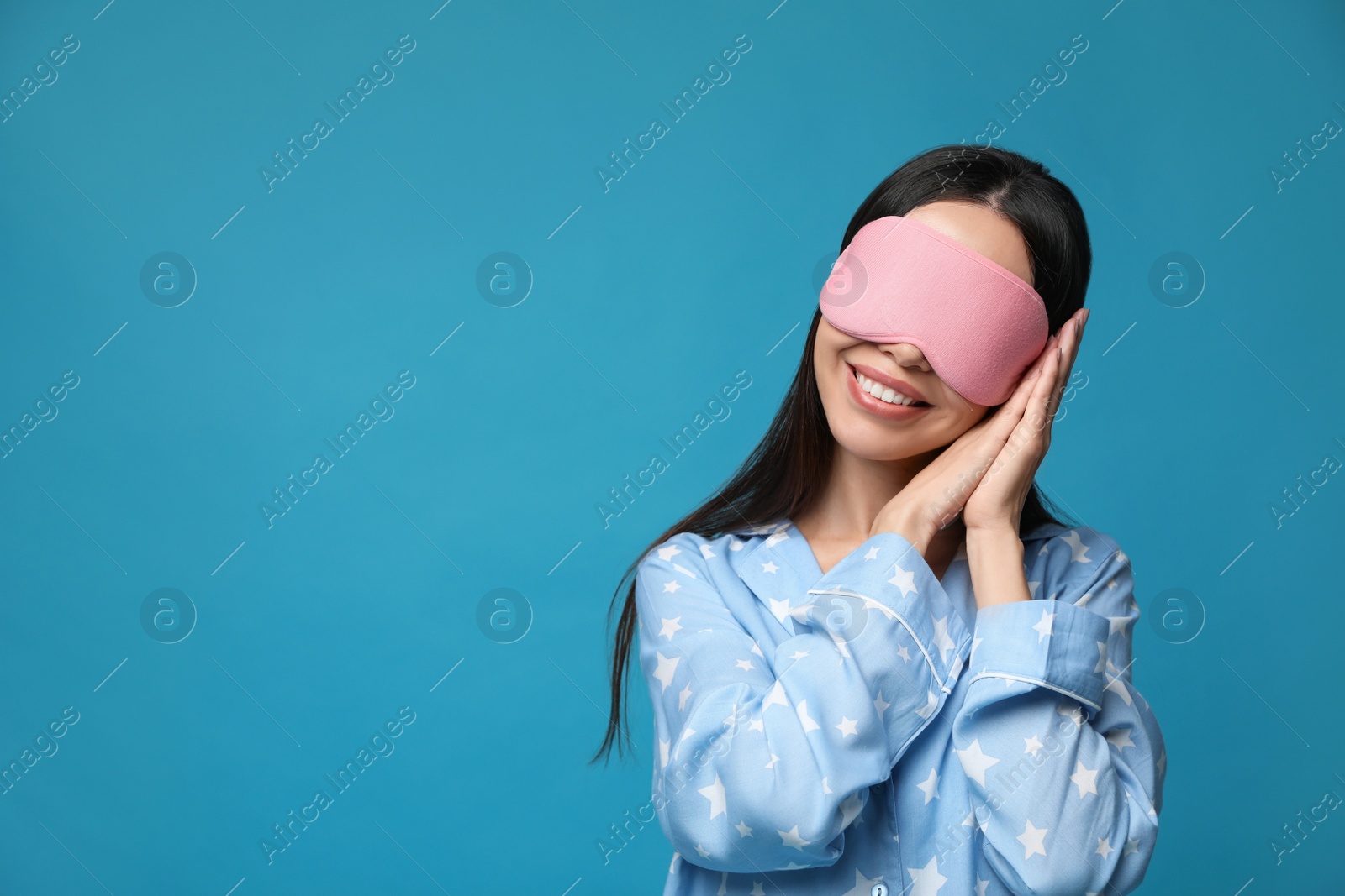 Photo of Young woman wearing pajamas and sleeping mask on blue background, space for text. Bedtime