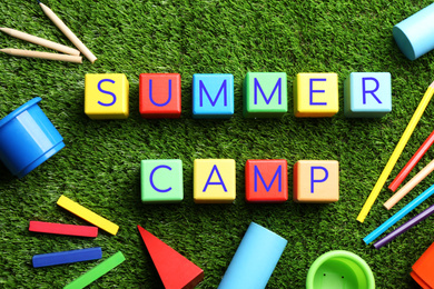 Flat lay composition with phrase SUMMER CAMP made of colorful cubes on green grass