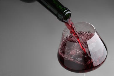 Photo of Pouring tasty red wine in glass at gray table, closeup. Space for text