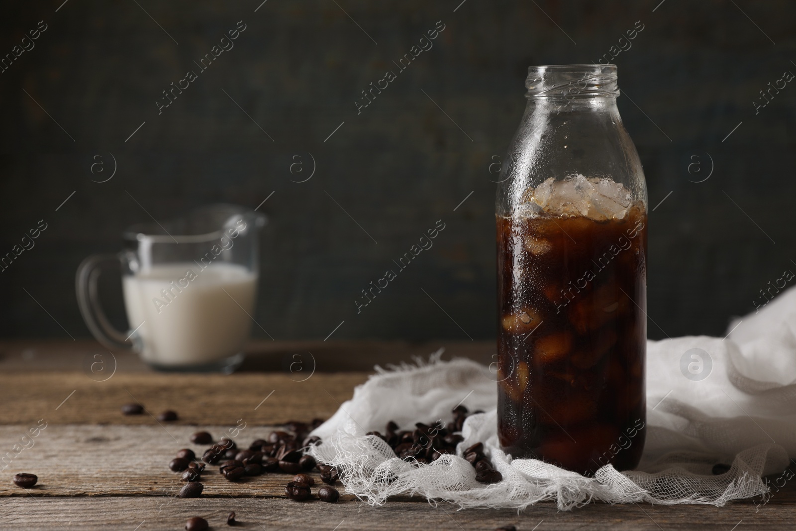 Photo of Delicious iced coffee in glass bottle near beans on wooden table, closeup. Space for text