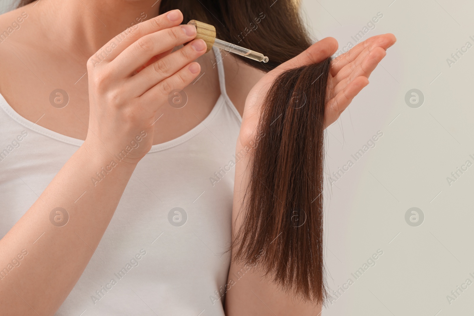 Photo of Woman applying essential oil onto hair on blurred background, closeup