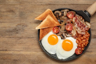 Photo of Serving pan of fried eggs, mushrooms, beans, bacon, tomatoes and toasted bread on wooden table, top view with space for text. Traditional English breakfast