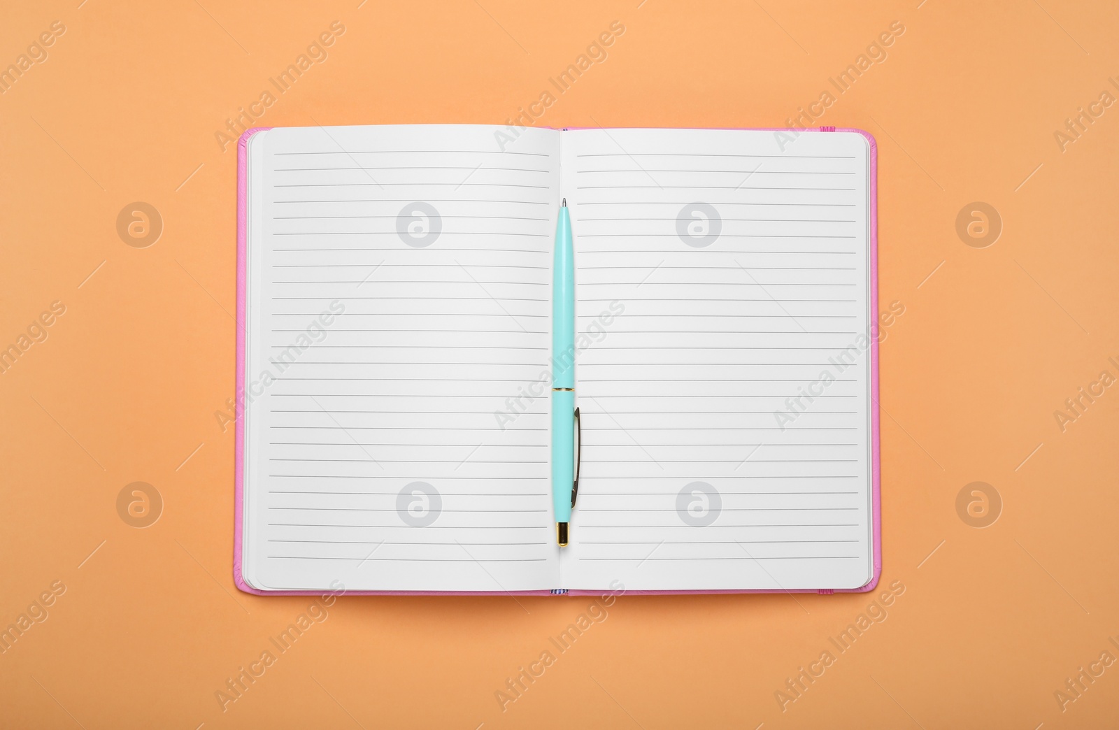 Photo of Open office notebook and pen on pale orange background, top view