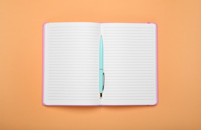 Photo of Open office notebook and pen on pale orange background, top view