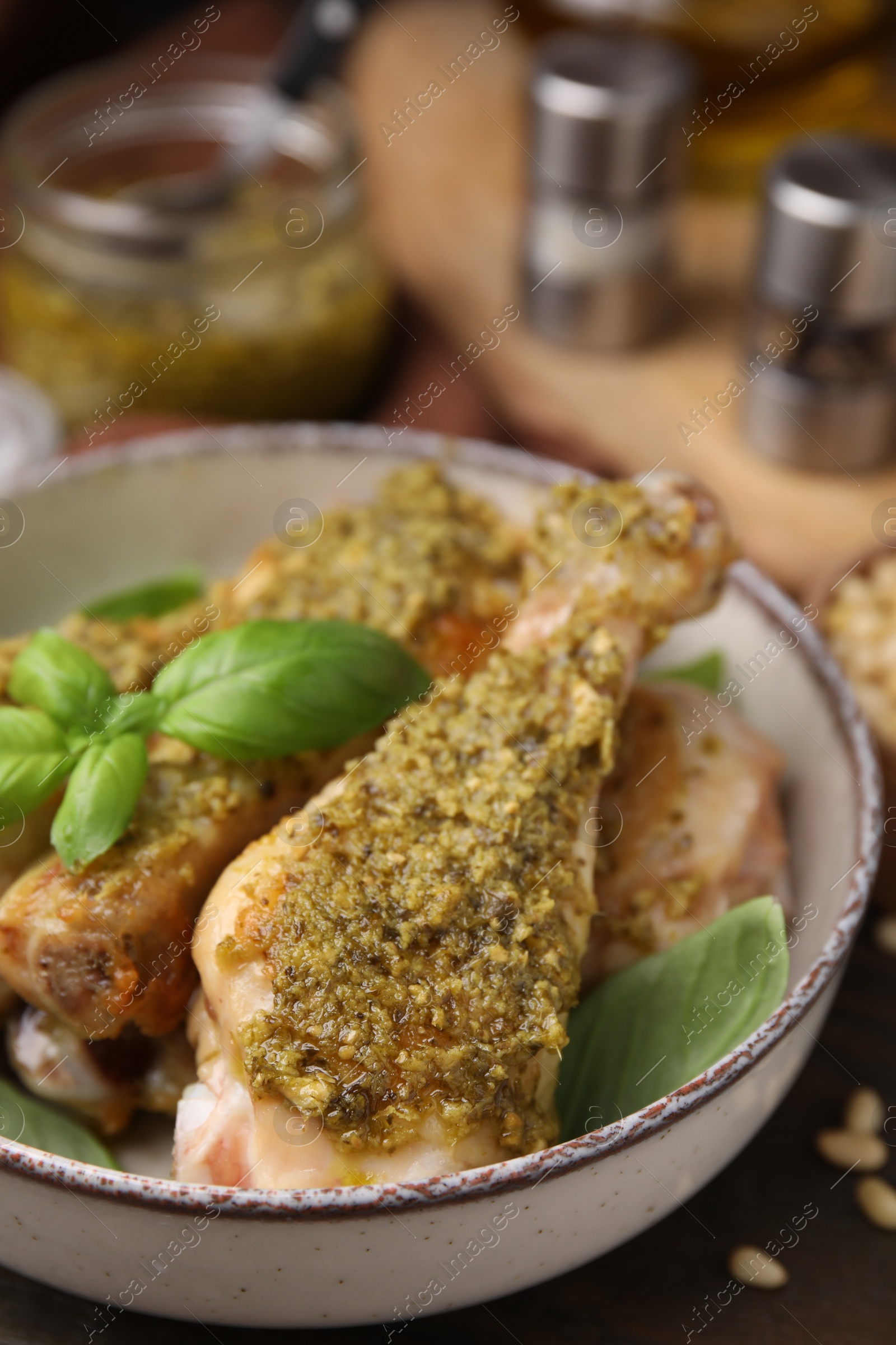 Photo of Delicious fried chicken drumsticks with pesto sauce and basil in bowl on table, closeup