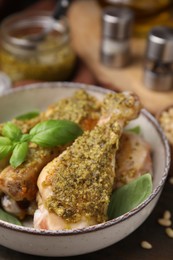 Photo of Delicious fried chicken drumsticks with pesto sauce and basil in bowl on table, closeup