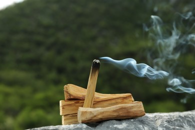 Photo of Burning palo santo stick on stone surface outdoors, closeup