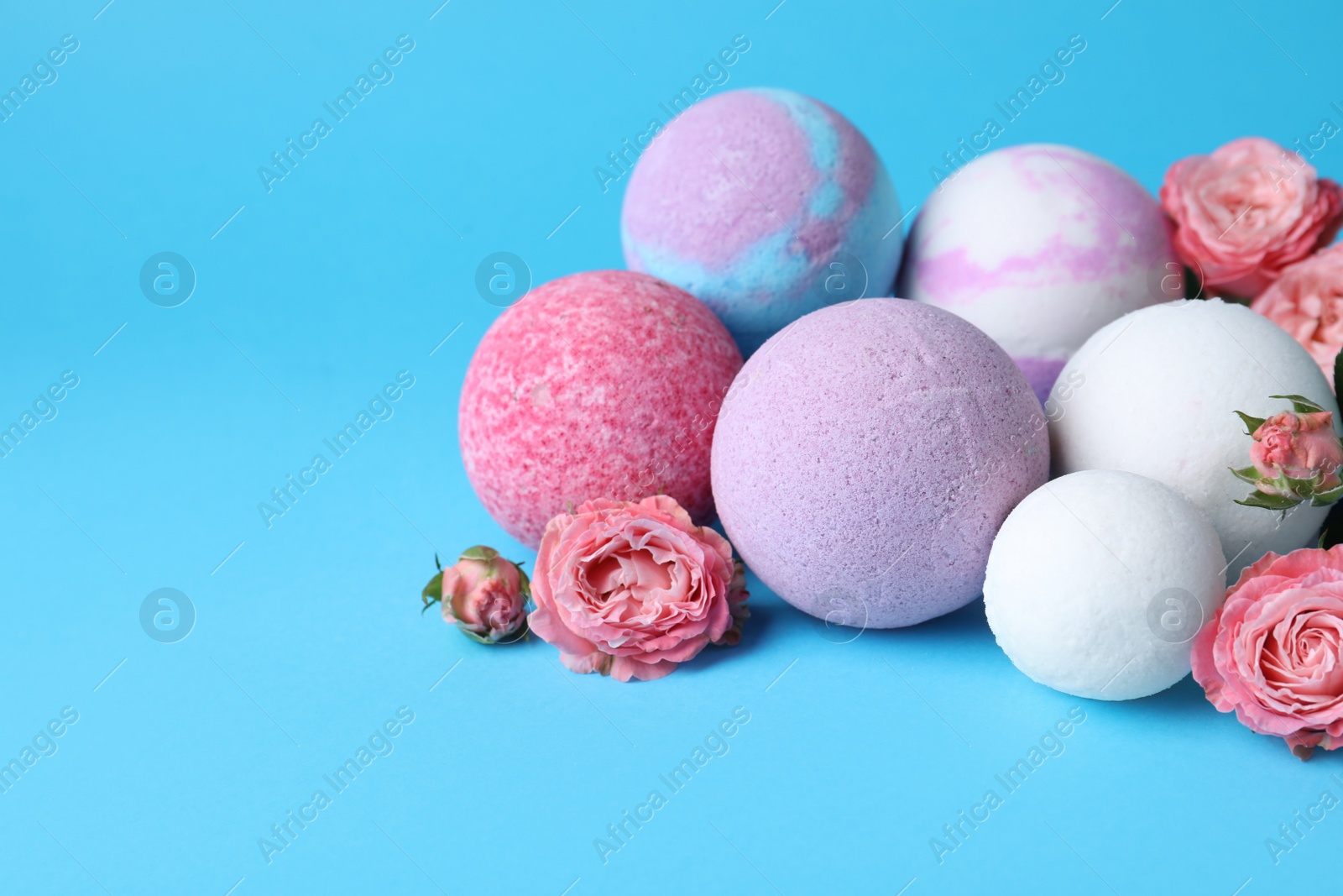 Photo of Colorful bath bombs and beautiful roses on light blue background, space for text