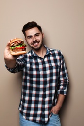 Handsome man eating tasty burger on color background