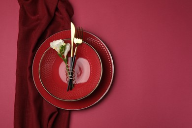 Stylish table setting with cutlery and floral decor on pink background, top view. Space for text