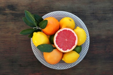 Bowl with different citrus fruits and leaves on wooden table, top view