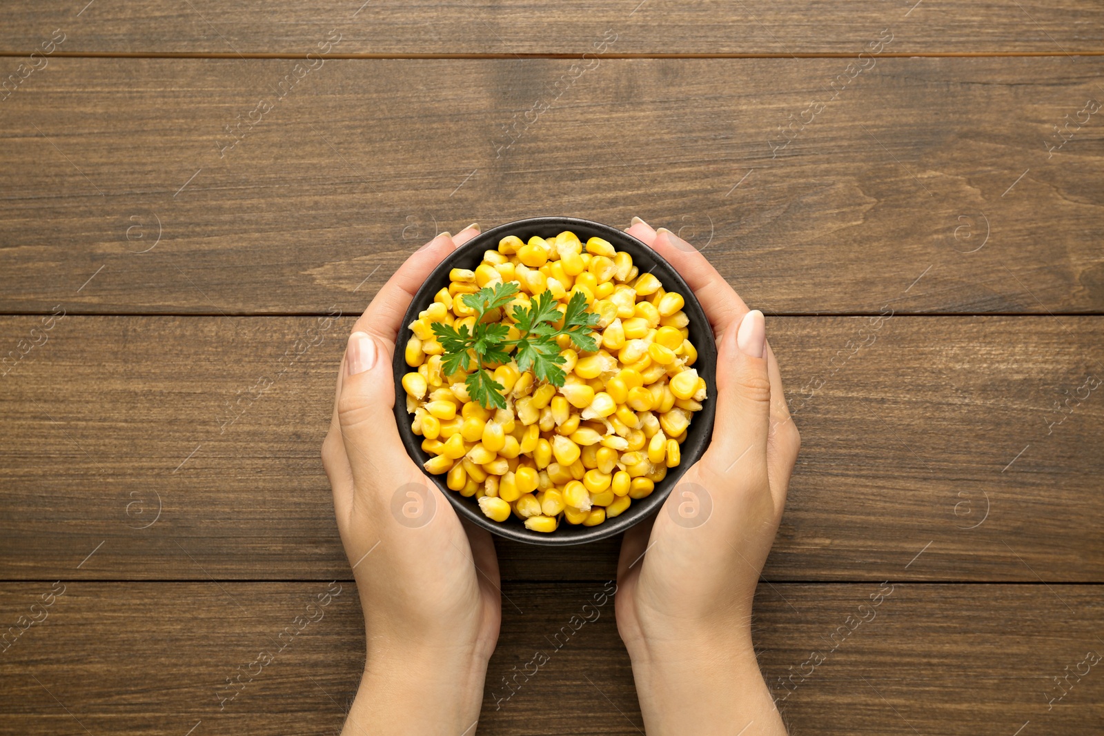 Photo of Woman holding bowl with tasty boiled corn at wooden table, top view