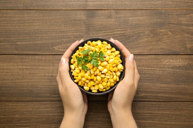 Woman holding bowl with tasty boiled corn at wooden table, top view