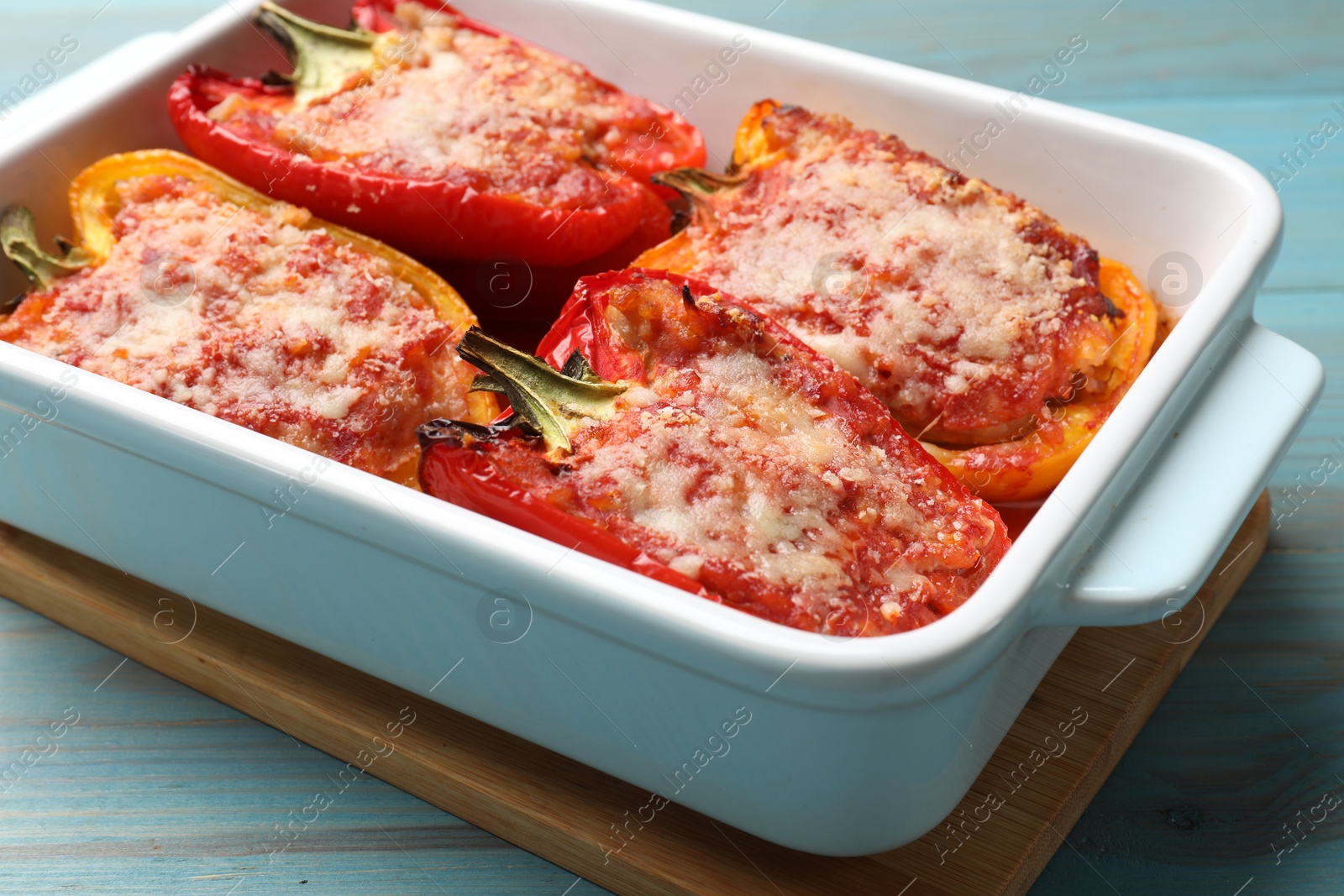 Photo of Tasty stuffed peppers in dish on light blue wooden table, closeup