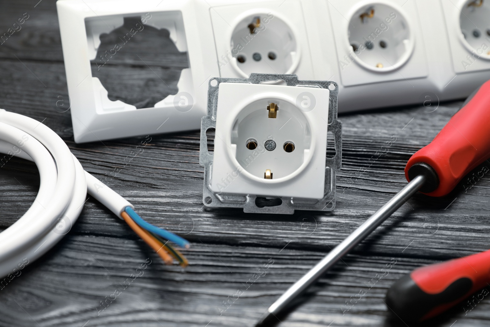 Photo of Electrician's tools and power sockets on black wooden table