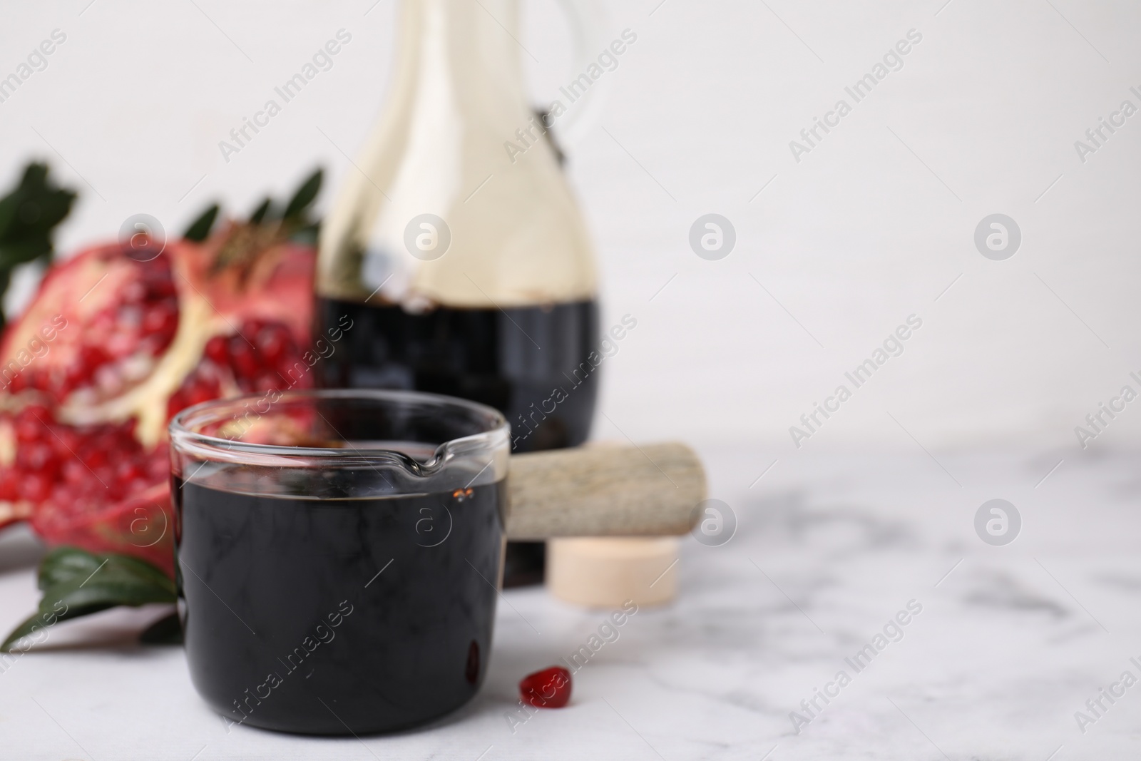 Photo of Tasty pomegranate sauce on white marble table, closeup. Space for text