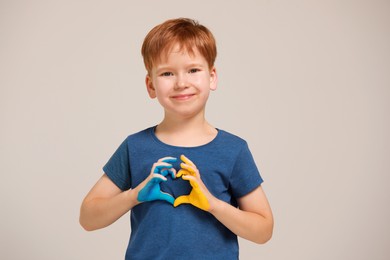 Photo of Little boy making heart with his hands painted in Ukrainian flag colors on light grey background. Love Ukraine concept