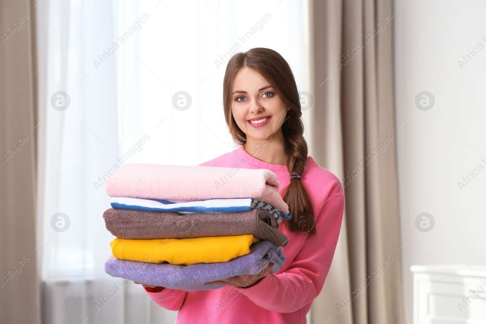 Photo of Happy young woman holding clean laundry at home