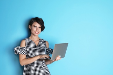 Young woman with modern laptop on color background