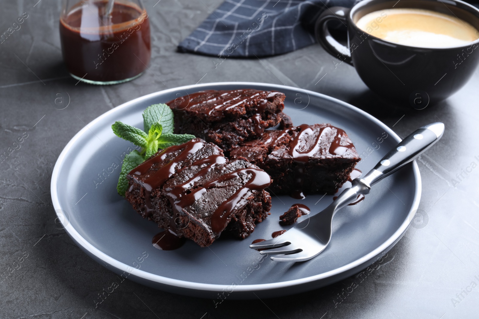 Photo of Delicious chocolate brownies with sweet syrup and mint served on grey table