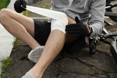 Photo of Man applying bandage onto his knee near bicycle outdoors, closeup