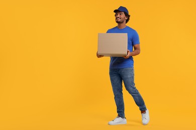 Photo of Happy courier with parcel on orange background, space for text