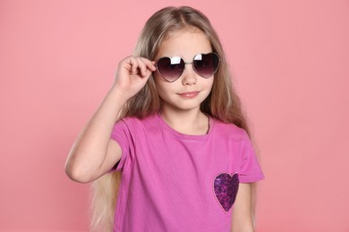 Photo of Girl wearing stylish sunglasses in shape of hearts on pink background