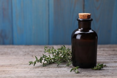 Bottle of thyme essential oil and fresh plant on wooden table, space for text