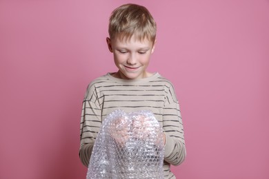 Photo of Boy popping bubble wrap on pink background. Stress relief