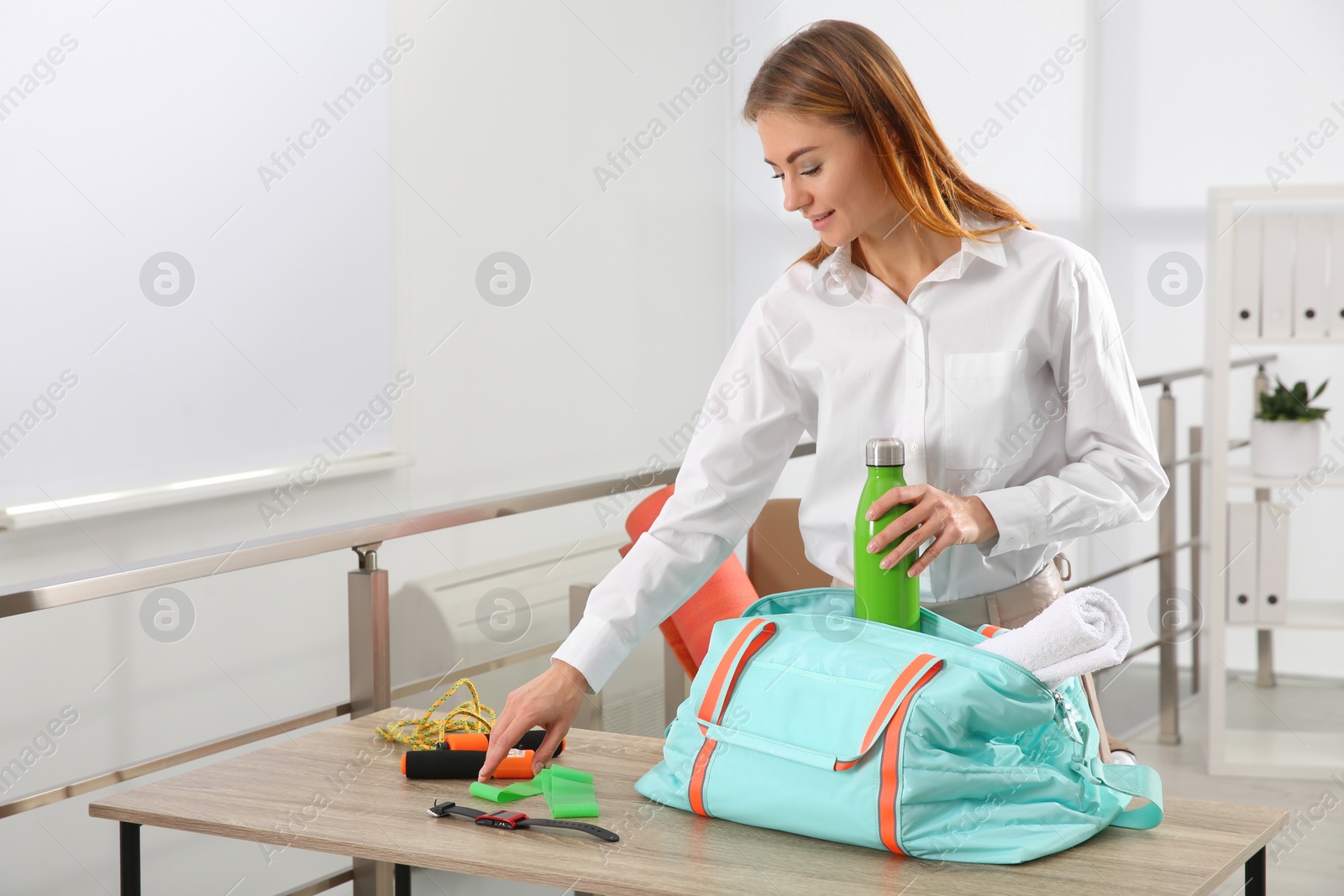 Photo of Businesswoman packing sports stuff for training into bag in office