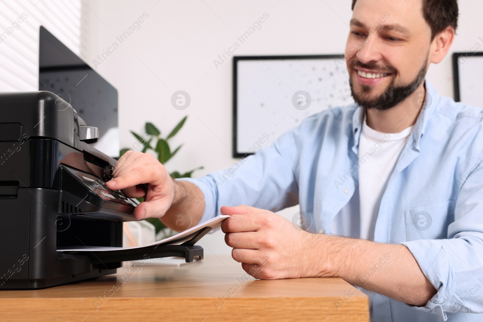 Photo of Man using modern printer at wooden table indoors, selective focus