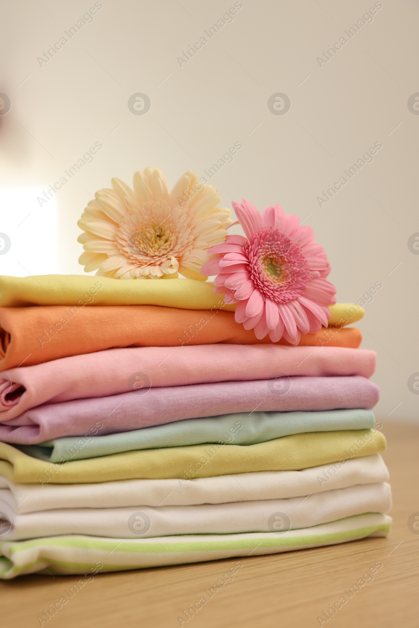 Photo of Stack of clean clothes and flowers on wooden table, closeup