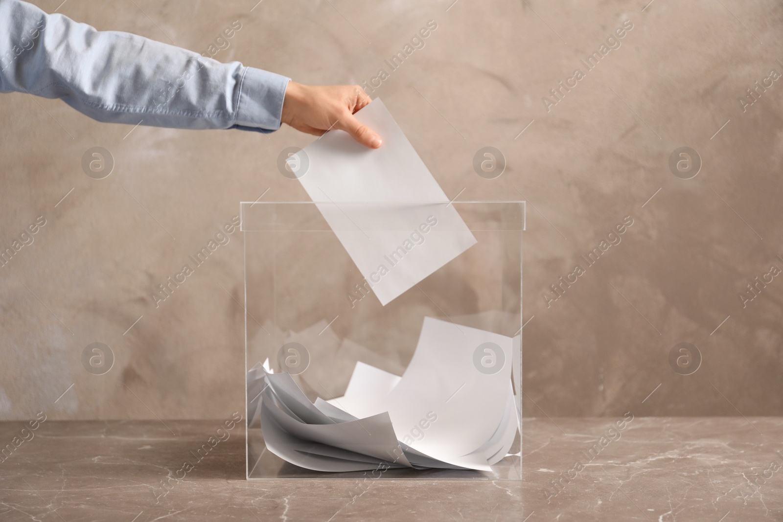 Photo of Man putting his vote into ballot box on color background, closeup