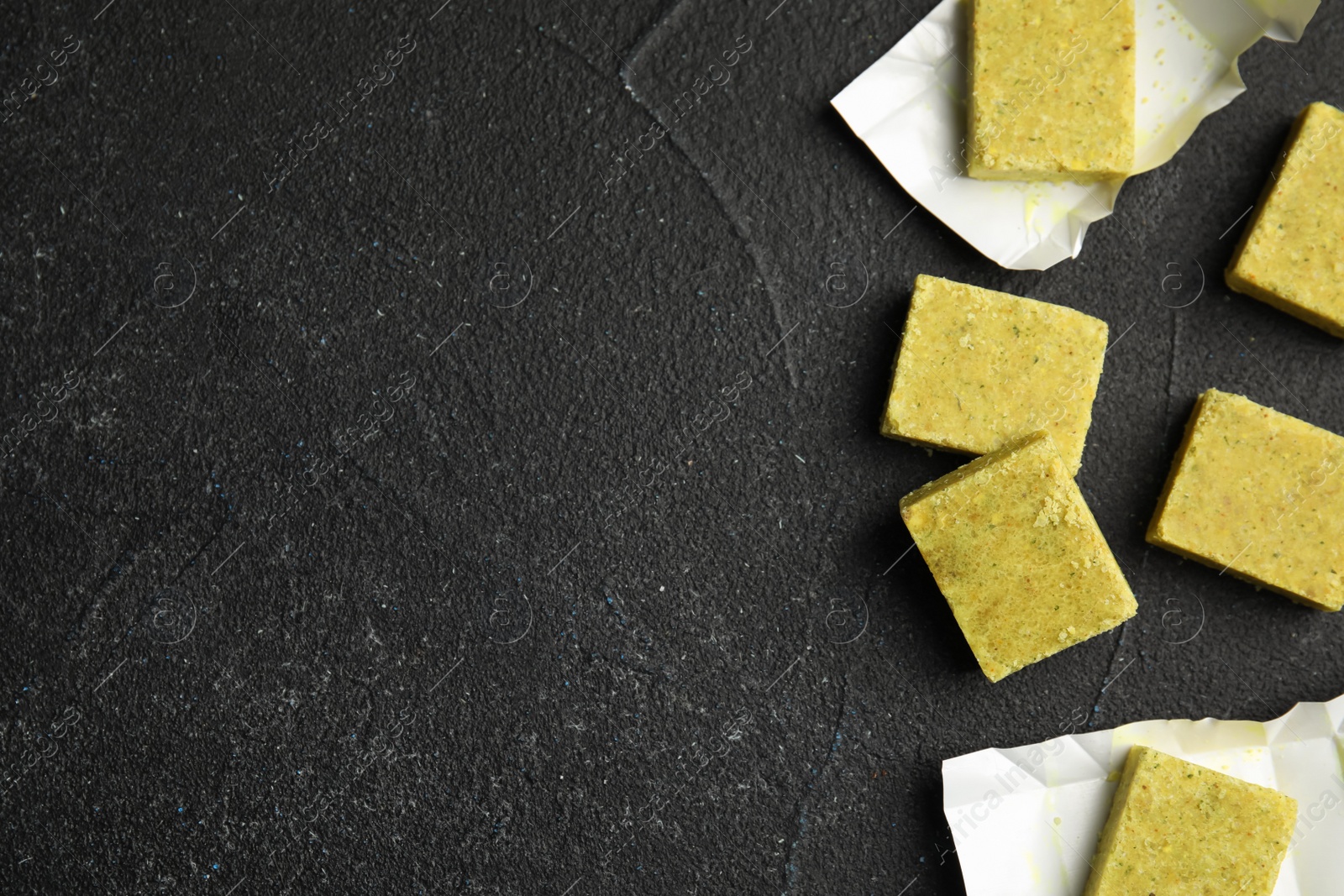 Photo of Aromatic natural bouillon cubes on black table, flat lay. Space for text