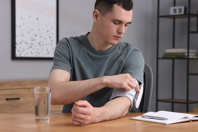 Young man measuring his blood pressure with tonometer at wooden table indoors