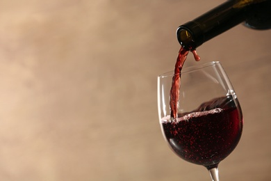 Photo of Pouring red wine into glass from bottle against blurred beige background, closeup. Space for text