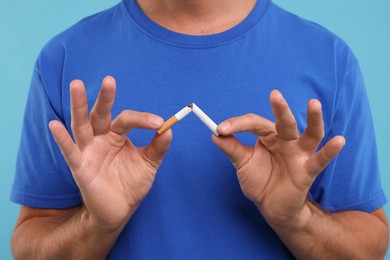Photo of Stop smoking concept. Man breaking cigarette on light blue background, closeup