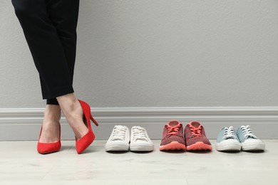 Photo of Businesswoman in high heel shoes standing near different comfortable sneakers indoors, closeup