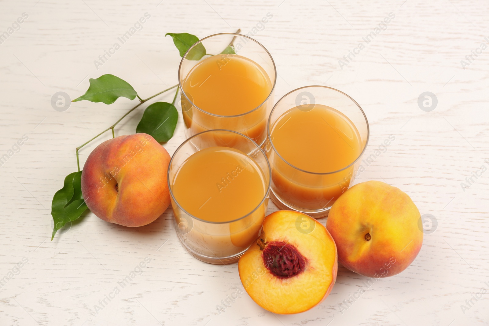 Photo of Glasses of delicious peach juice, fresh fruits and leaves on white wooden table, above view