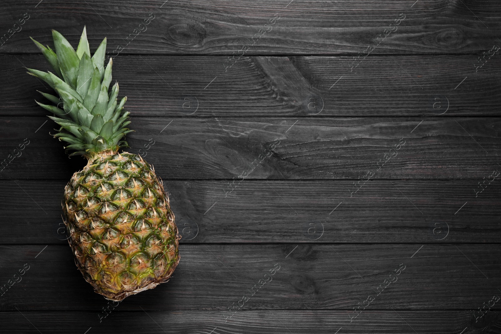 Photo of Whole ripe pineapple on black wooden table, top view. Space for text