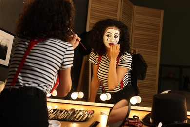 Photo of Young woman applying mime makeup near mirror indoors