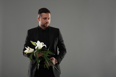 Sad man with white lilies on grey background, space for text. Funeral ceremony