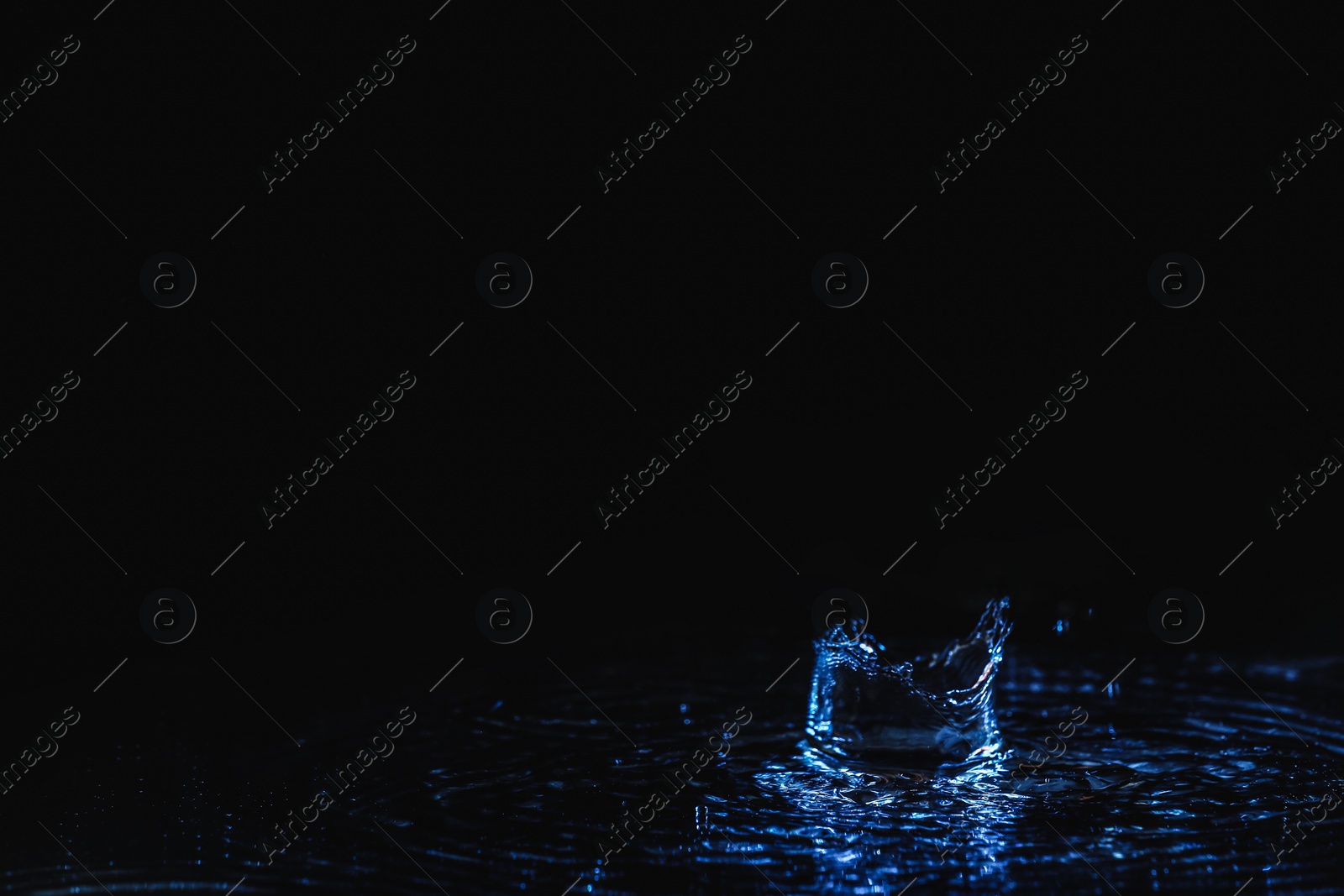 Photo of Rain drop falling down into puddle on dark background, space for text