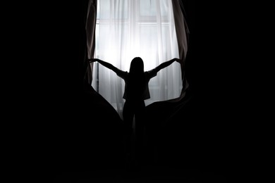 Image of Silhouette of woman opening curtains at home, back view