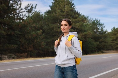 Happy young woman with backpack on road near forest